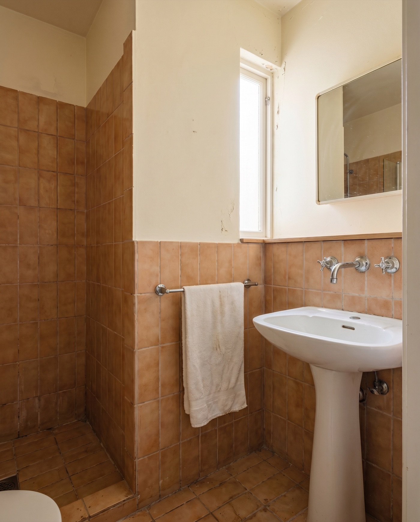 Current bathroom with dated paint, an old tap and an old mirror, same tiles as the after shot