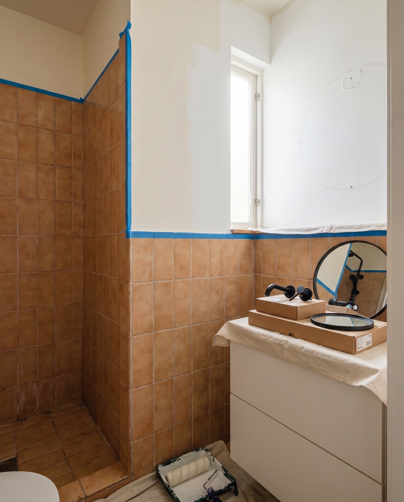 Bathroom mid-refresh with masking tape along the tiles and a new tap ready to fit